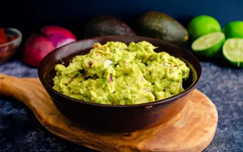 Miseczka guacamole z awokado, cebulą i limonką na drewnianej desce.
