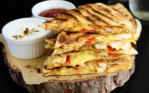 Stos pysznych kawałków quesadilli z kurczakiem, roztopionym serem i papryką, podane z dipami.