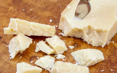 Kawałki sera Grana Padano na drewnianej desce. Czy Grana Padano to parmezan? Ten twardy ser dojrzewa długo, podobnie jak parmezan.