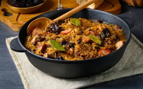 Pyszny bigos w żeliwnym naczyniu, z widocznymi kawałkami mięsa, śliwkami i liśćmi laurowymi. Idealne danie, gdy zastanawiasz się, jakie mięso do bigosu wybrać.