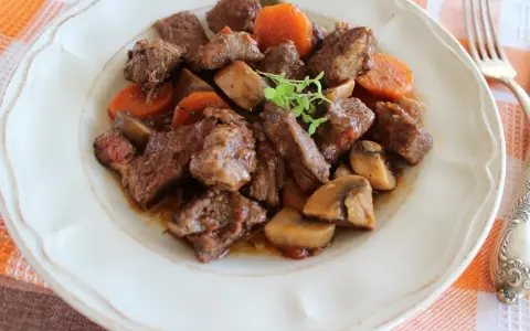 Pyszne wołowina po burgundzku z pieczarkami i marchewką, podana na talerzu.