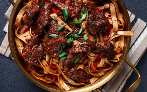 Pyszne wolowina po seczuańsku z makaronem, papryczkami chili i szczypiorkiem w złotej misie.