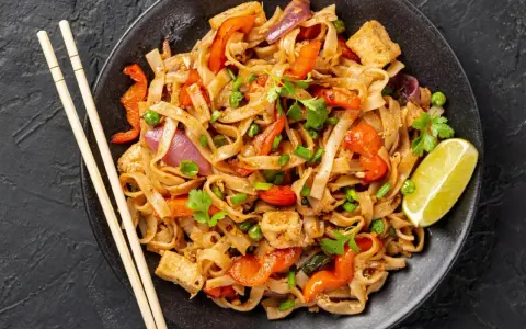 Pyszny pad thai z kurczakiem, warzywami i makaronem ryżowym, udekorowany kolendrą i ćwiartką limonki.