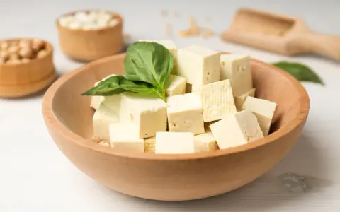 Kostki tofu w drewnianej misce z bazylią. Czy tofu można jeść na surowo? Tak, to świetna baza do sałatek i przekąsek.