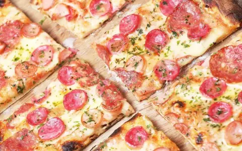 Kawałki pysznej pizzy na cienkim cieście z kiełbasą i serem, posypane ziołami.