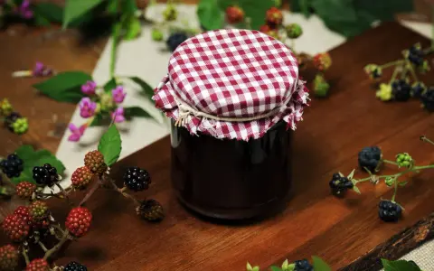 Słoik domowego dżemu z jeżyn, otoczony świeżymi owocami. Idealny sposób, by zachować smak lata i pokazać, co można zrobić z jeżyn.
