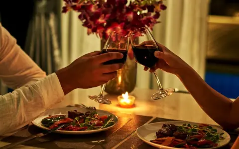 Romantyczna kolacja dla dwojga przy świecach. Dwie pary kieliszków z czerwonym winem unoszą się w geście toastu.