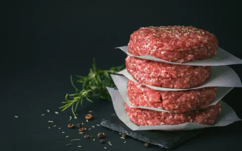Stos świeżego, mielonego mięsa na burgery, przyprawionego ziołami i pieprzem, gotowe do grillowania.