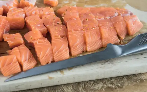 Świeży, pokrojony łosoś do sushi, doprawiony, leży na desce obok noża. Idealny łosoś do sushi.
