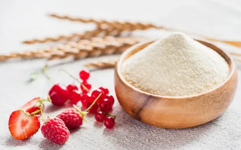 Miseczka z semoliną, obok świeże owoce: maliny, truskawki, porzeczki i kłosy zbóż. Semolina co to? To mąka z pszenicy durum.