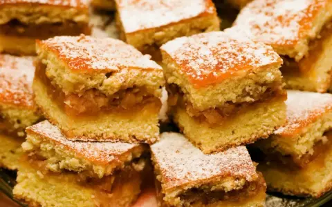 Szybkie ciasto z jabłkami, pokrojone w kostkę i posypane cukrem pudrem, wygląda apetycznie.