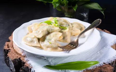 Pyszne pierogi ze szpinakiem i serem, udekorowane czosnkiem niedźwiedzim, na białym talerzu.