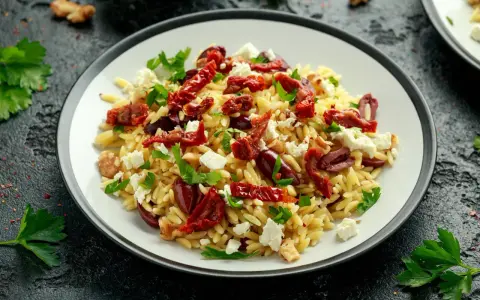 Pyszna sałatka z makaronem orzo, z suszonymi pomidorami, oliwkami, fetą i natką pietruszki.