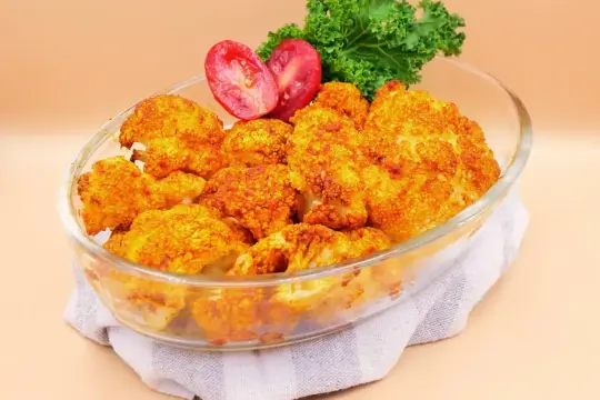 Zapiekany kalafior w piekarniku, który smakuje jak niebo w gębie. Podany w szklanej misie z pomidorkami i liśćmi jarmużu.