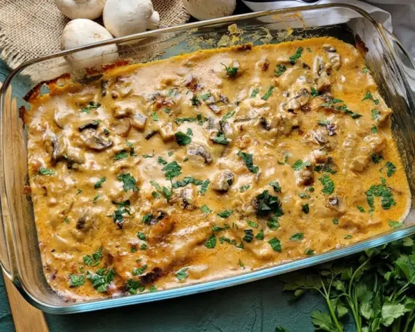 Pyszny schab w sosie grzybowym, zapieczony w naczyniu żaroodpornym, posypany świeżą natką pietruszki.