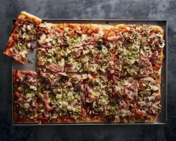 Pyszna pizza domowa przepis na blachę z szynką, pieczarkami i oliwkami. Idealna na rodzinne spotkanie.