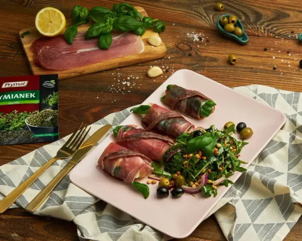 Roladki z szynką parmeńską, ziół, anchois i serka, podane z sałatką z rukoli, oliwek i orzeszków pinii.