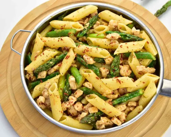 Penne z kurczakiem i szparagami, posypane papryką. Pyszne danie na obiad.