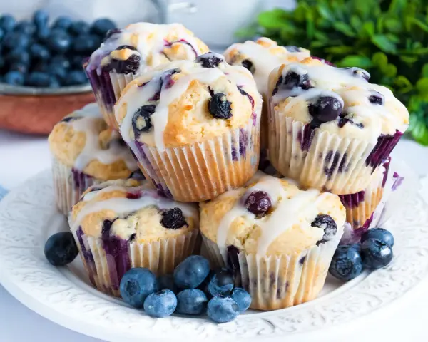 Stos pysznych muffinek z borówkami, polanych lukrem, ozdobionych świeżymi borówkami. Idealne na śniadanie lub deser.