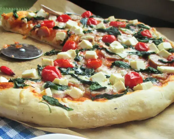 Pyszna pizza ze szpinakiem, pomidorkami koktajlowymi i kostkami sera feta. Idealna na szybki obiad.