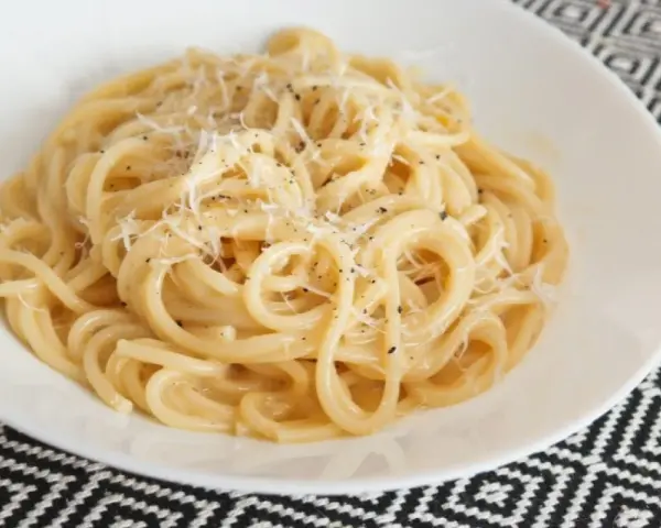 Pyszna carbonara bez śmietany, z parmezanem i pieprzem, podana w białej misce na wzorzystym obrusie.