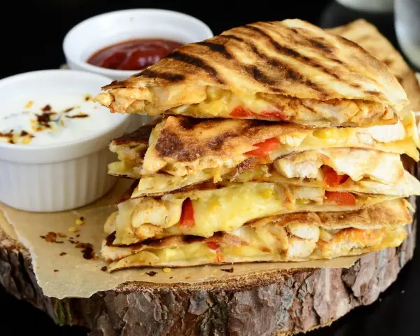 Stos pysznych kawałków quesadilli z kurczakiem, roztopionym serem i papryką, podane z dipami.