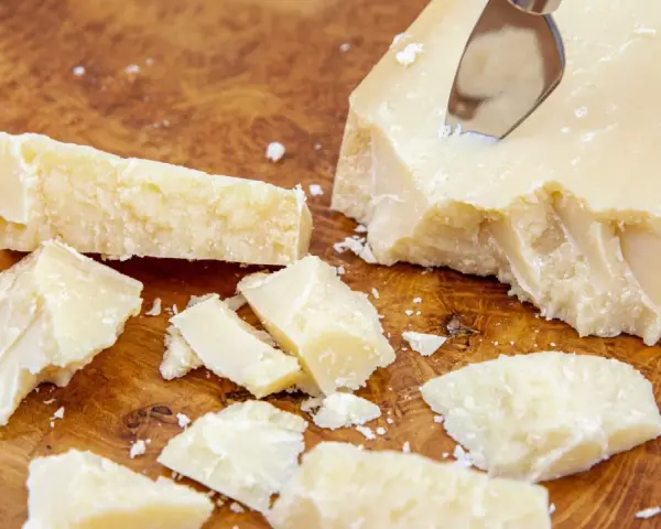 Kawałki sera Grana Padano na drewnianej desce. Czy Grana Padano to parmezan? Ten twardy ser dojrzewa długo, podobnie jak parmezan.