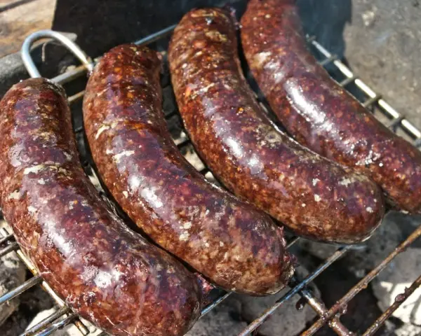 Cztery soczyste kaszanki z grilla pieką się na ruszcie, uwalniając apetyczny aromat.