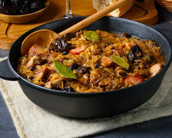 Pyszny bigos w żeliwnym naczyniu, z widocznymi kawałkami mięsa, śliwkami i liśćmi laurowymi. Idealne danie, gdy zastanawiasz się, jakie mięso do bigosu wybrać.