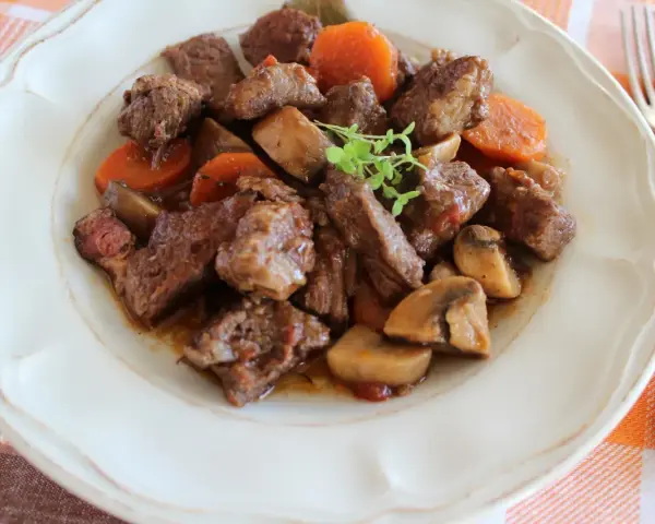 Pyszne wołowina po burgundzku z pieczarkami i marchewką, podana na talerzu.