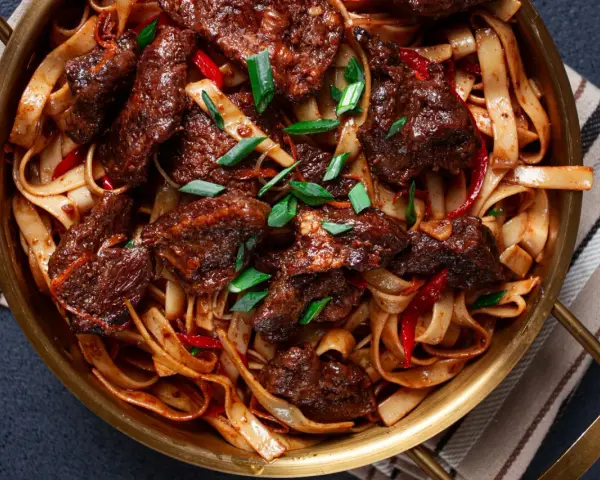 Pyszne wolowina po seczuańsku z makaronem, papryczkami chili i szczypiorkiem w złotej misie.
