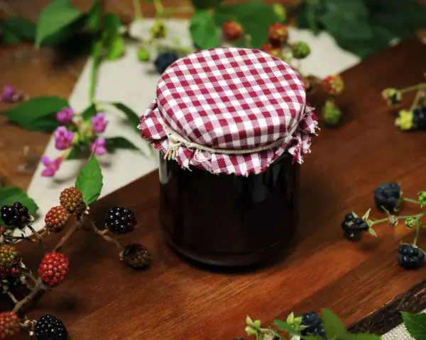 Słoik domowego dżemu z jeżyn, otoczony świeżymi owocami. Idealny sposób, by zachować smak lata i pokazać, co można zrobić z jeżyn.
