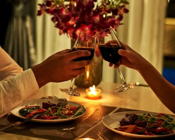 Romantyczna kolacja dla dwojga przy świecach. Dwie pary kieliszków z czerwonym winem unoszą się w geście toastu.