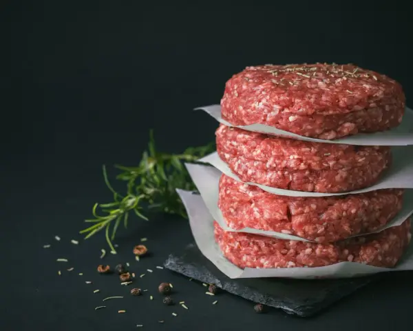 Stos świeżego, mielonego mięsa na burgery, przyprawionego ziołami i pieprzem, gotowe do grillowania.