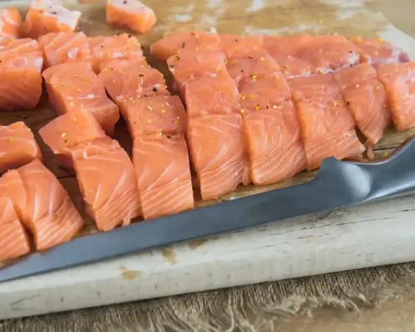 Świeży, pokrojony łosoś do sushi, doprawiony, leży na desce obok noża. Idealny łosoś do sushi.