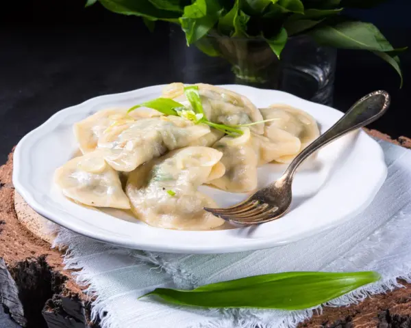 Pyszne pierogi ze szpinakiem i serem, udekorowane czosnkiem niedźwiedzim, na białym talerzu.