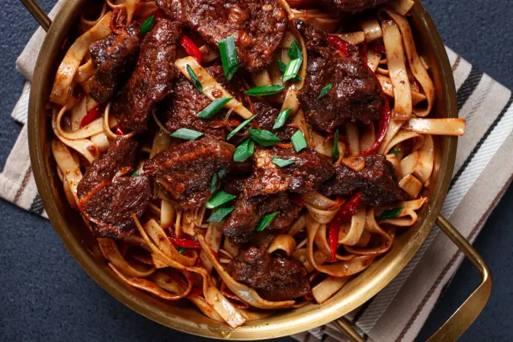 Pyszne wolowina po seczuańsku z makaronem, papryczkami chili i szczypiorkiem w złotej misie.
