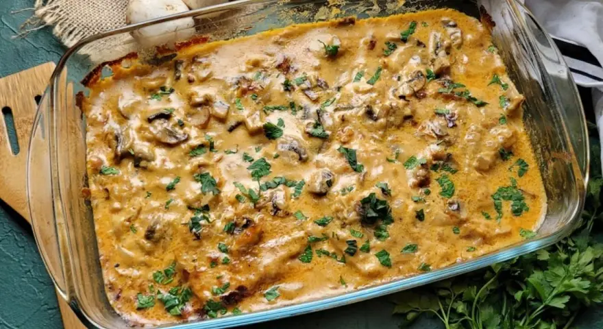 Pyszny schab w sosie grzybowym, zapieczony w naczyniu żaroodpornym, posypany świeżą natką pietruszki.