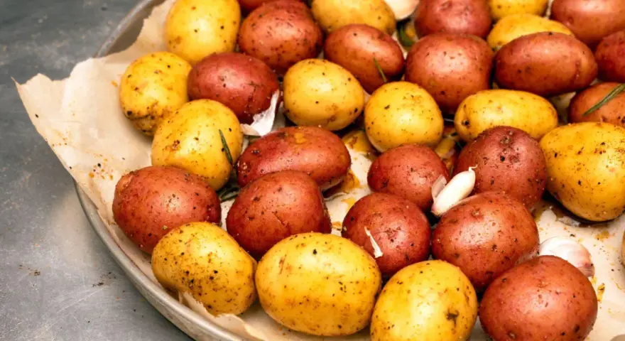 Ziemniaki z ogniska, czerwone i żółte, przyprawione czosnkiem i ziołami, gotowe do pieczenia.