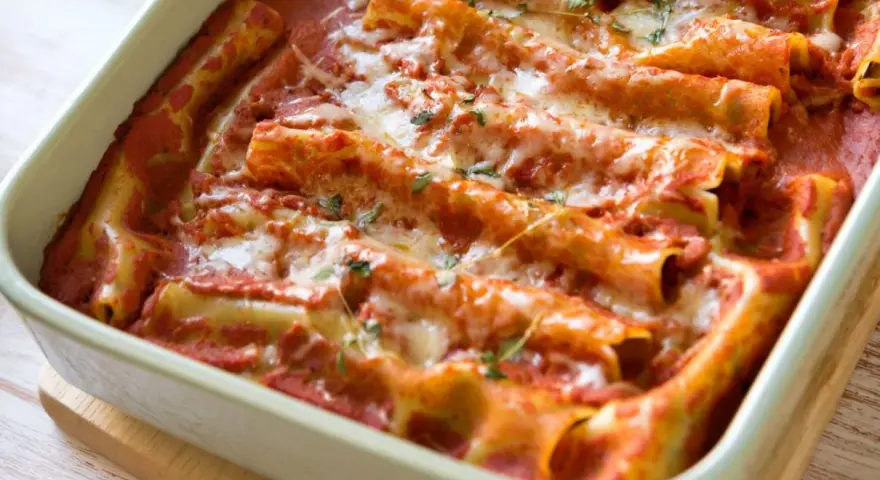 Pyszne cannelloni ze szpinakiem zapieczone w sosie pomidorowym, posypane serem i ziołami.