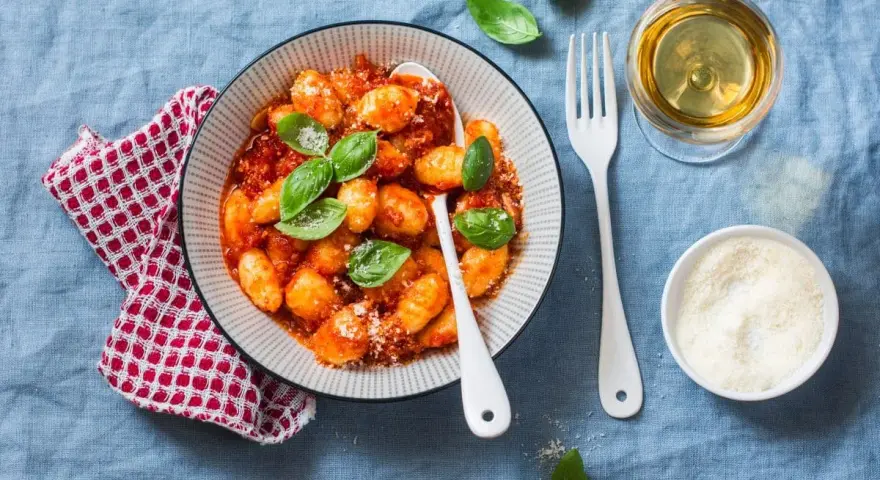 Pyszne gnocchi w sosie pomidorowym, posypane parmezanem. Idealne z kieliszkiem białego wina.