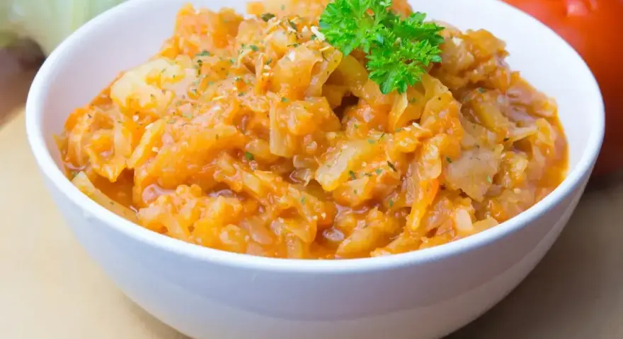 Pyszny bigos ze słodkiej kapusty, duszony z pomidorami i przyprawami, udekorowany natką pietruszki.