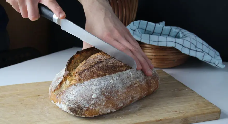 Ręka kroi pyszny, świeżo upieczony chleb z garnka. Chrupiąca skórka i miękki środek zachęcają do spróbowania.