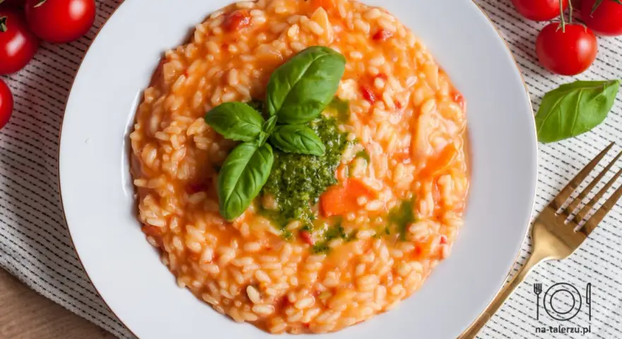Pyszne risotto z pomidorami, udekorowane bazylią i pesto, czeka na talerzu. Obok świeże pomidorki i złoty widelec.