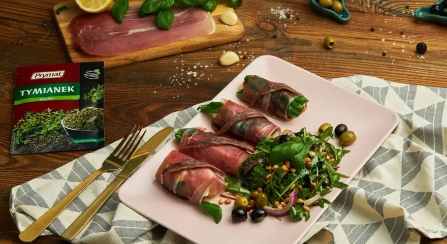 Roladki z szynką parmeńską, ziół, anchois i serka, podane z sałatką z rukoli, oliwek i orzeszków pinii.