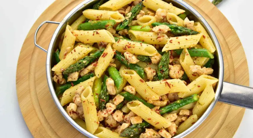 Penne z kurczakiem i szparagami, posypane papryką. Pyszne danie na obiad.