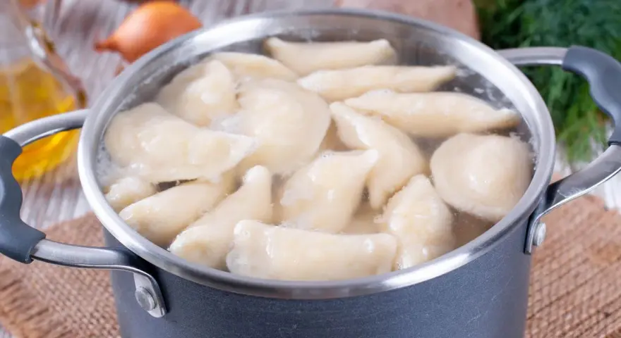 Pierogi gotują się w garnku. Woda wrze, a pierożki wypływają na powierzchnię. Czas gotowania pierogów jest kluczowy dla ich smaku.