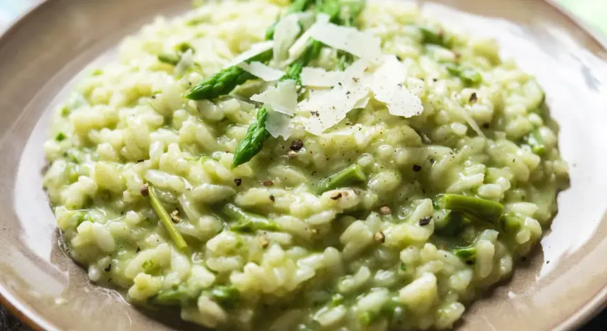 Kremowe risotto ze szparagami, posypane płatkami parmezanu i świeżo mielonym pieprzem.