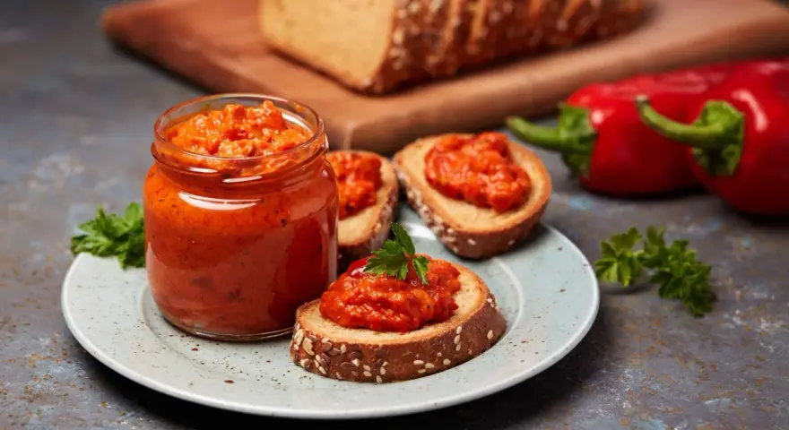 Słoik ajvaru i pieczywo z pastą. Ajvar do czego? Idealny na kanapki, dodatek do mięs i warzyw.