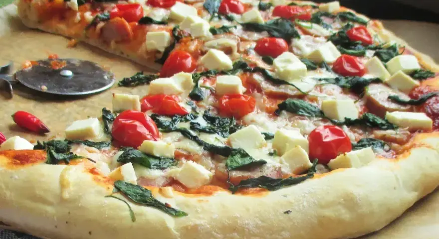 Pyszna pizza ze szpinakiem, pomidorkami koktajlowymi i kostkami sera feta. Idealna na szybki obiad.